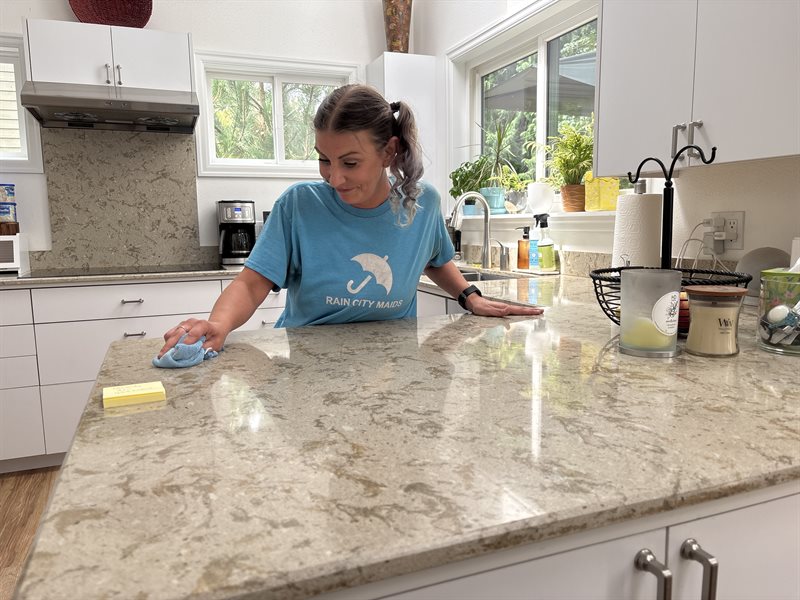 A Rain City Maids cleaner wiping a granite kitchen counter