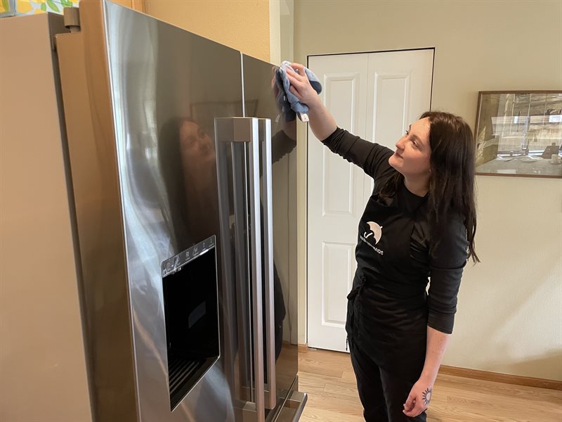 A Rain City Maids cleaner cleaning a refrigerator door