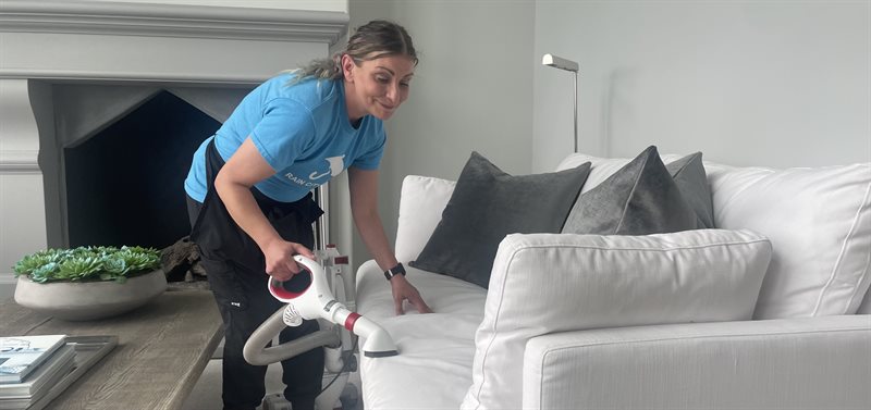 A Rain City Maids cleaner vacuuming a sofa