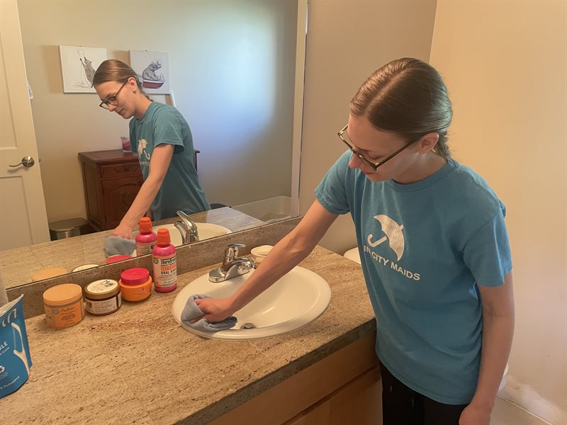 A Rain City Maids cleaner wiping a bathroom counter